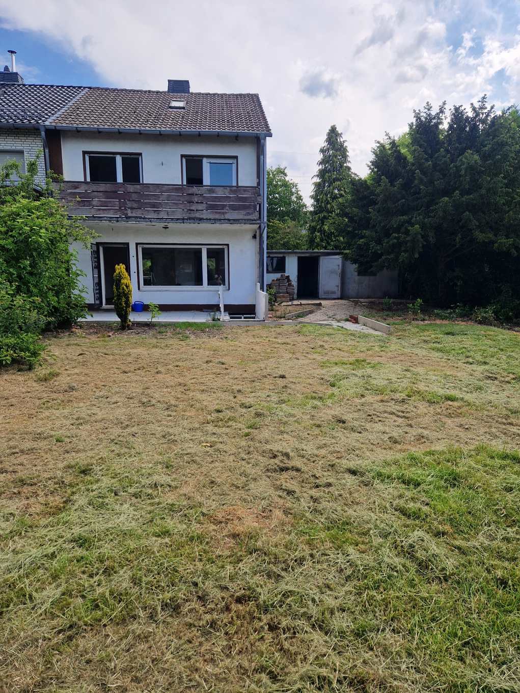 Zweistöckiges weißes Haus mit Ziegeldach, Fenstern und trockenem Rasen im Garten.